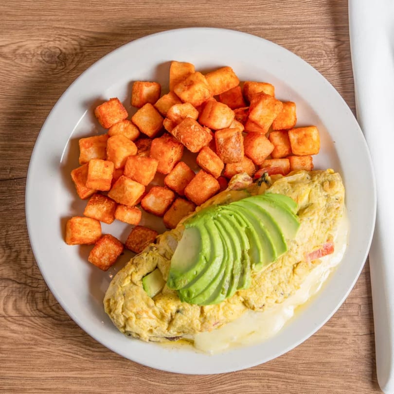 A breakfast plate with a cheese omelet topped with avocado slices and a side of crispy hash browns.