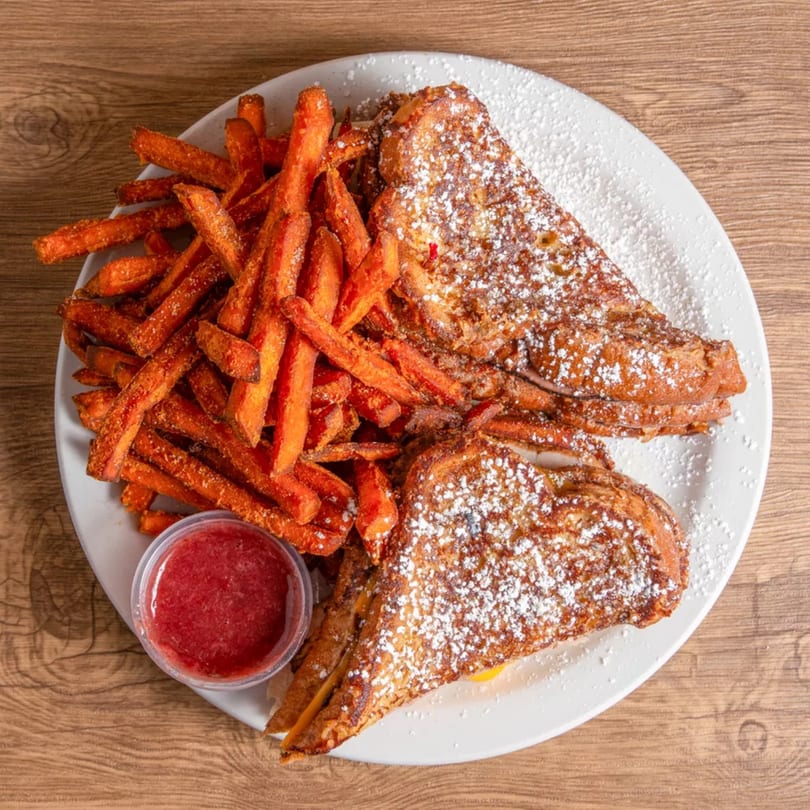 French toast triangles dusted with powdered sugar, sweet potato fries, and a side of strawberry sauce.