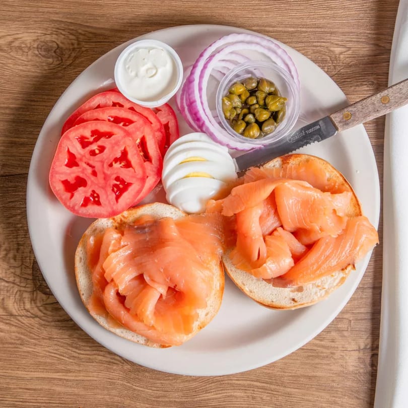 A bagel with lox, sliced tomatoes, red onion, capers, cream cheese, and hard-boiled egg.